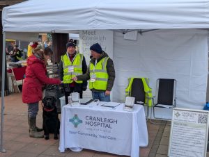 Two people in high viz jackets talking to a lady with a dog.