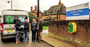 Four people standing behind a bus. Hospital sign in foreground. 