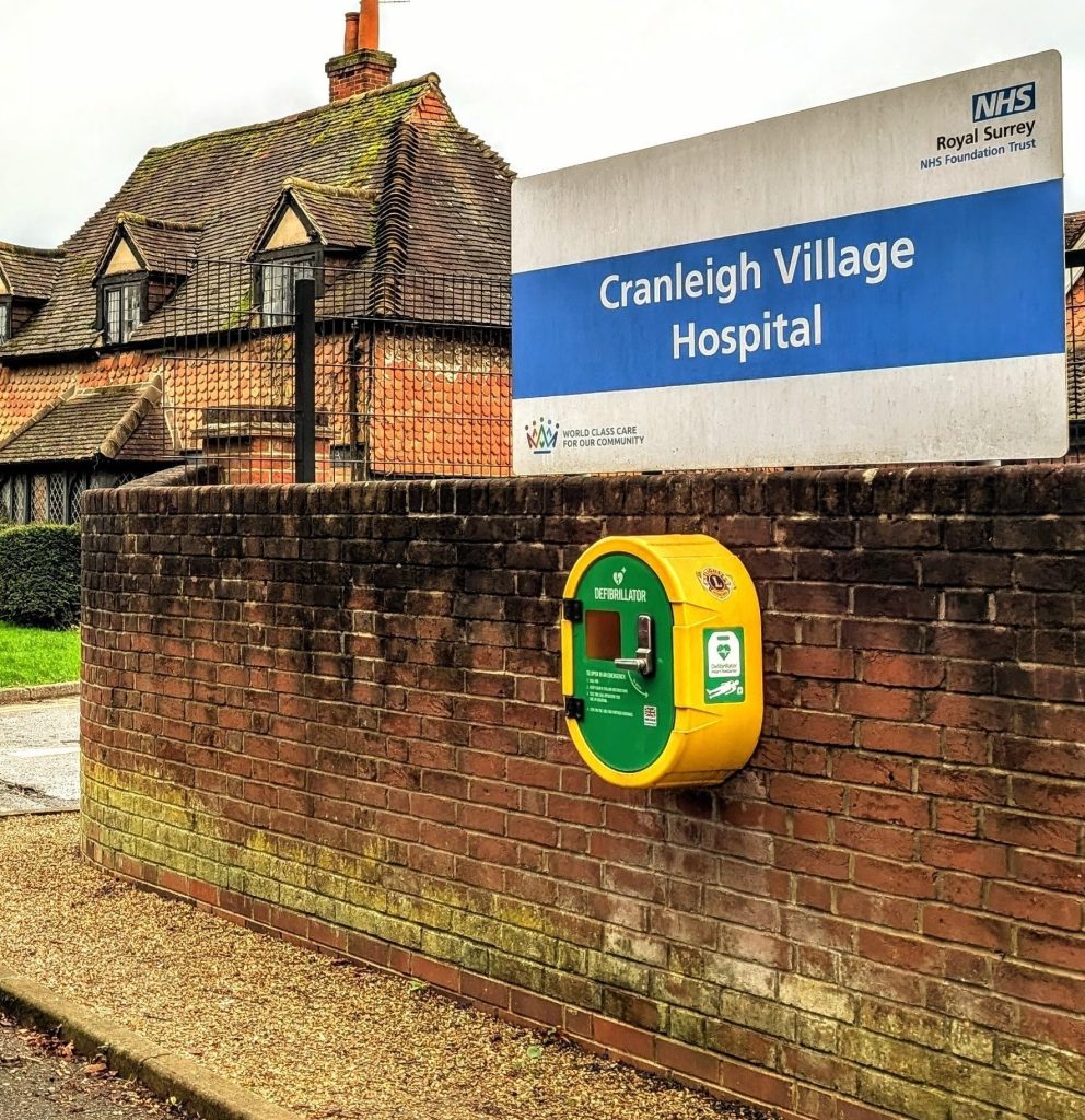 Defibrillator mounted on a wall beneath a hospital sign.