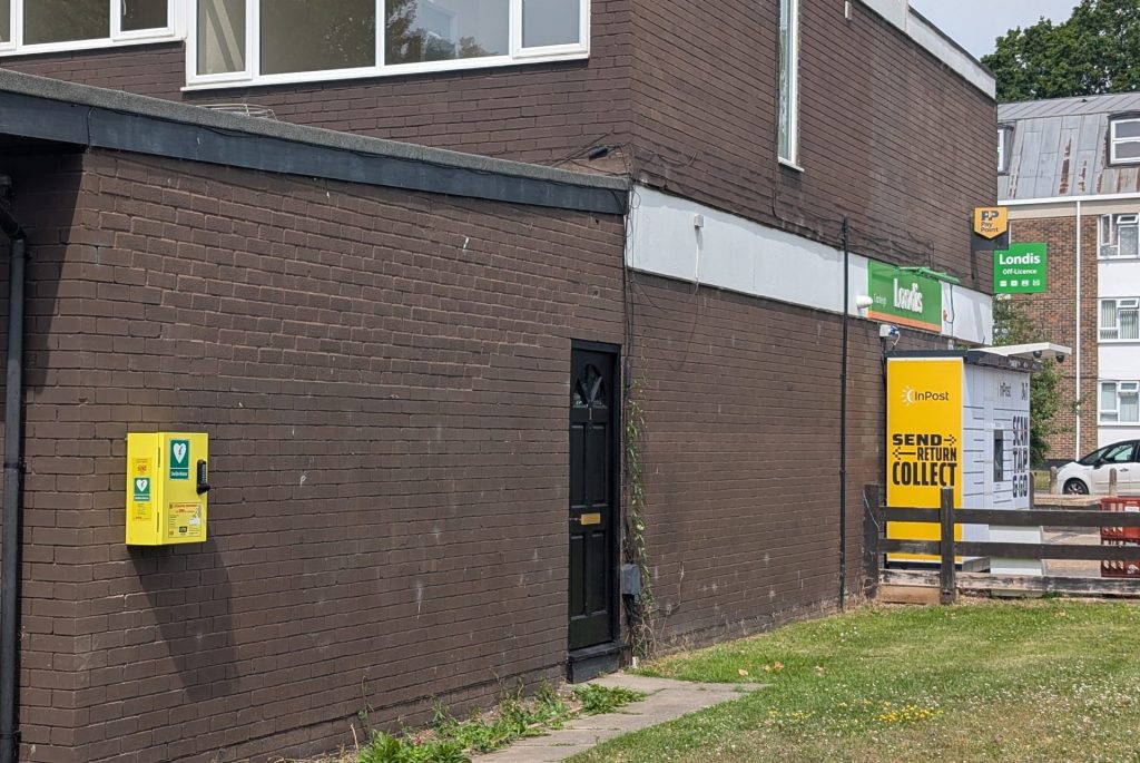 A defibrillator mounted on a brick wall outside a shop.