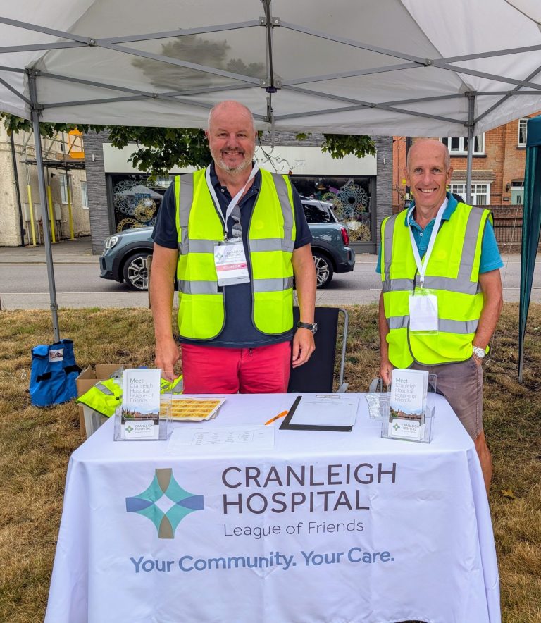 Two men in high viz jackets standing behind a table draped in a tablecloth.