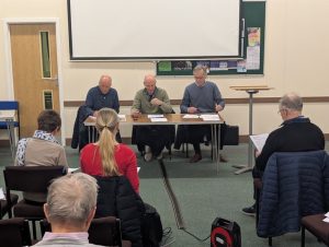 Three people sitting at a meeting table facing an audience. 