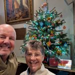 Man and woman in front of small decorated Christmas trees.